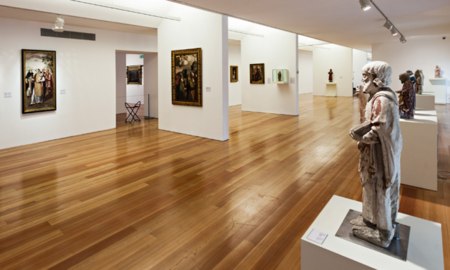 View of a clean, simple art museum gallery with paintings and sculpture.