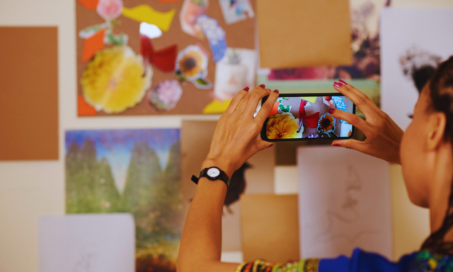 Over-the-shoulder view of a woman holding her phone up to works of art.