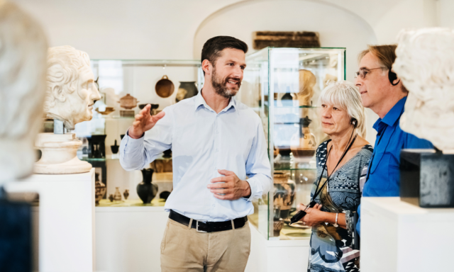 Museum docent speaking to a man and woman wearing headphones.