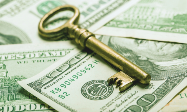 A golden key on top of a pile of American $100 bills.