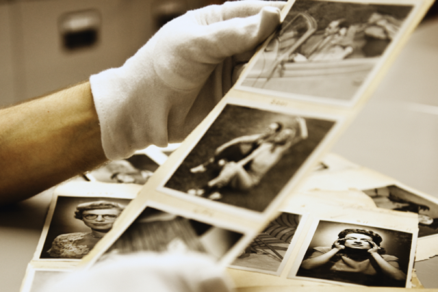 Hands in white gloves holding black and white archival photos