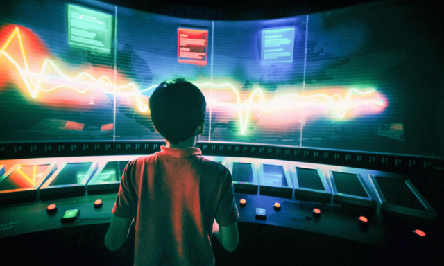 View from behind of a boy engaging with an interactive computer exhibit at a museum.