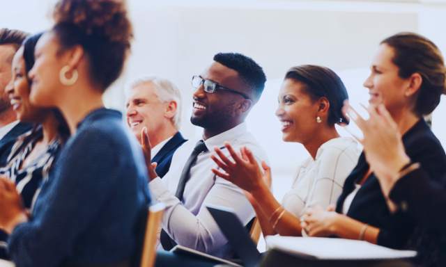 Diverse group of adults listening to a speaker at a conference.