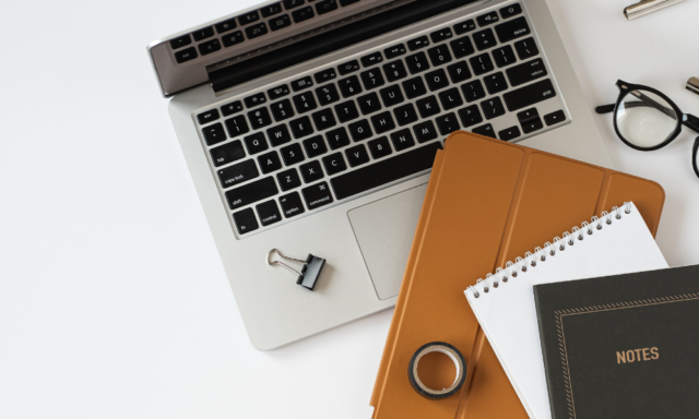 View from above of a laptop, portfolio, and notebooks on a desk.