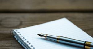 October 3 | Webinar: Interpretive Writing Strategies Blank spiral notebook with a fountain pen resting on it.