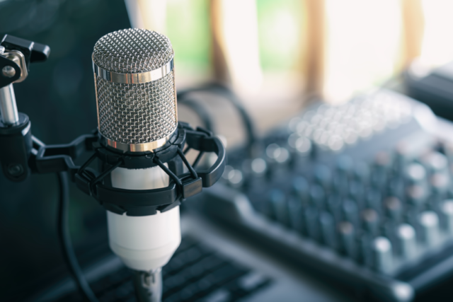 A microphone with podcasting gear in the background.