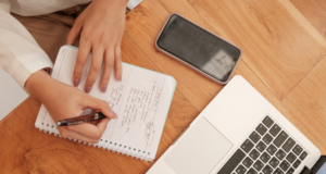 October 28 | Webinar: Engaging in Difficult Conversations: Tools for Connecting When Difference Creates Conflict View from above of a personal writing in a notebook with a cell phone and laptop nearby.