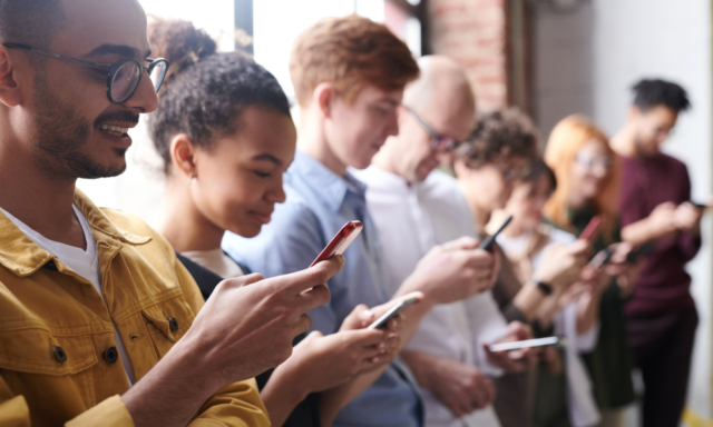 A group of people standing in a line looking at their phones