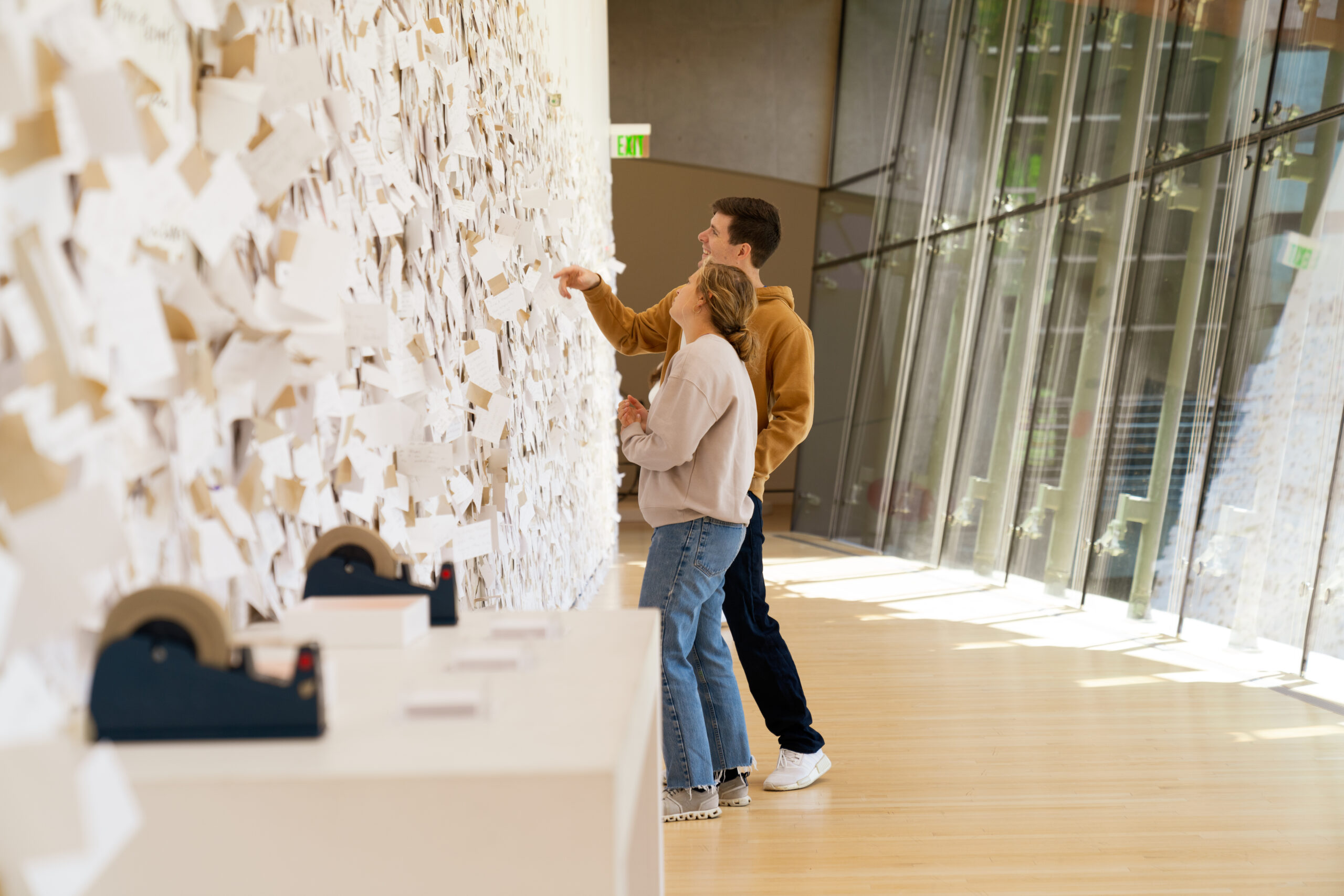 A man and woman standing in front of a wall of notes to mothers at Crystal Bridges Museum of American Art, part of My Mommy Is Beautiful.