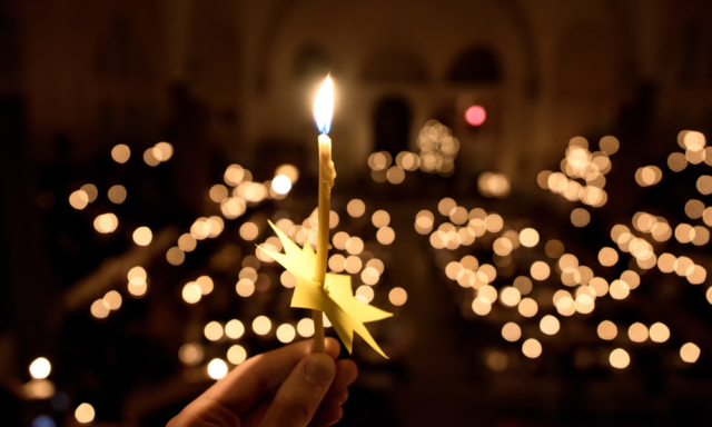 a hand holding a lit candle in front of twinkling white lights