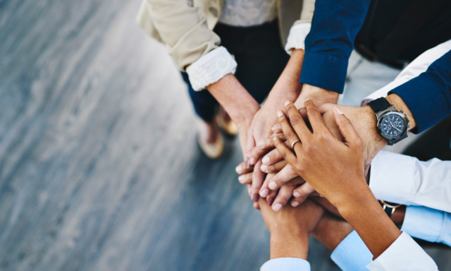 multiple peoples' hands joined in a stack to represent collaboration