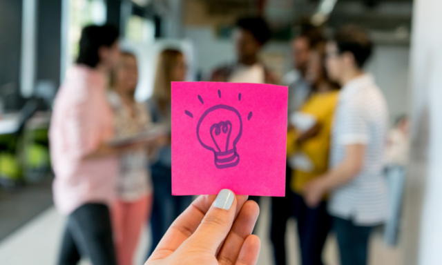 hand holding up a pink note with a light bulb drawn on it