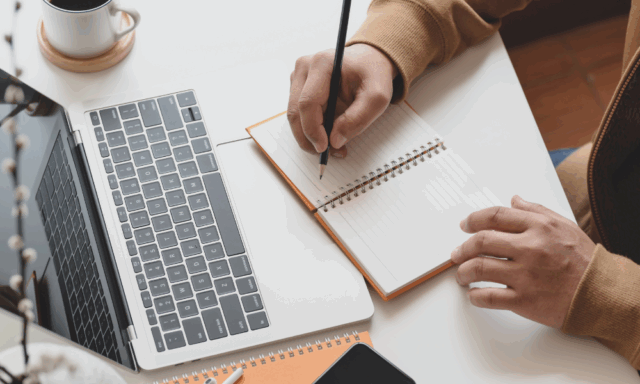overhead view of a person writing in a notebook in front of a laptop