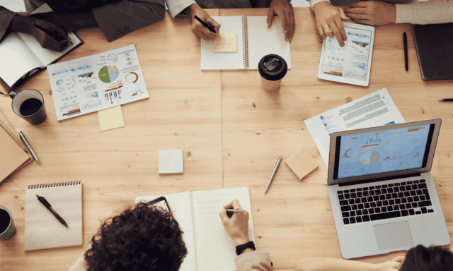 Overhead view of people at a business meeting with papers, notebooks, laptops on a table