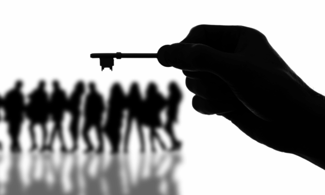 silhouette of a hand holding a key with a group of people in the background, also in silhouette