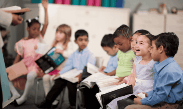a row of small children sitting in chairs and holding notebooks