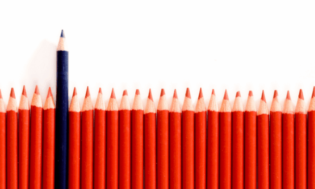 An even row of red pencils with one black pencil sticking up taller than the rest