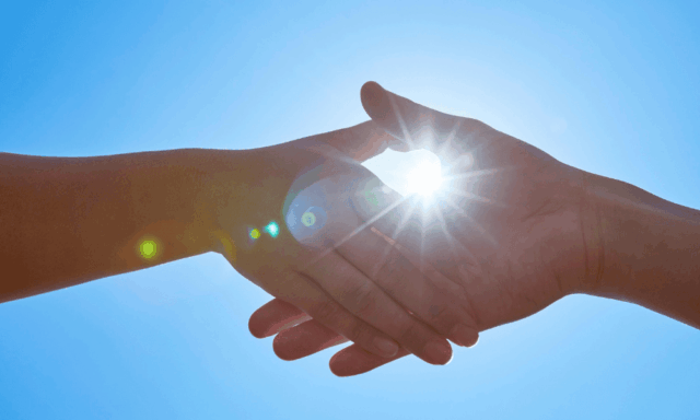 two hands meeting in a handshake with the sun shining through behind